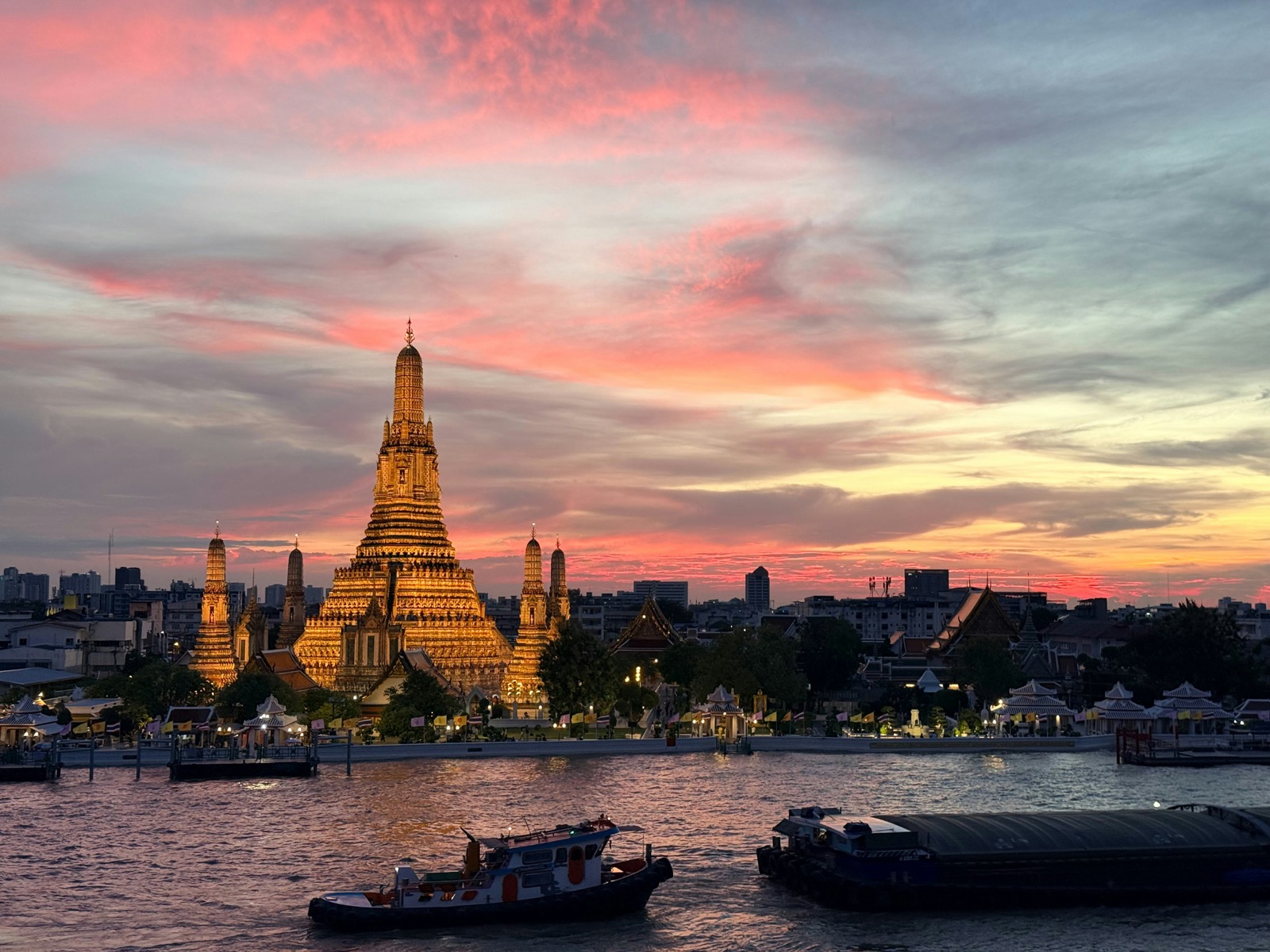 Osvetlený chrám Wat Arun pri rieke Chao Phraya v Bangkoku počas západu slnka