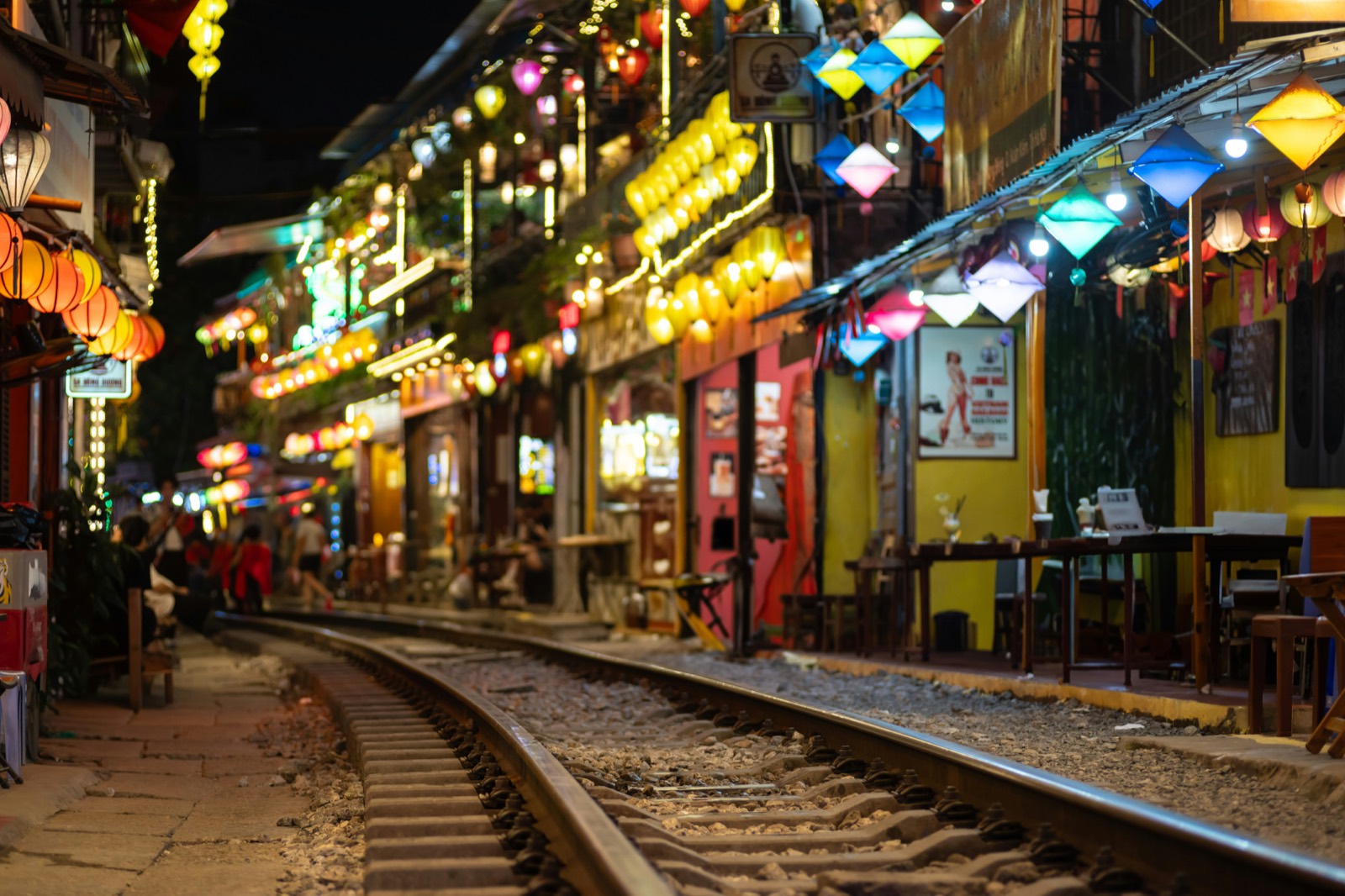 Večerná Train Street v Hanoji s farebnými lampiónmi a osvetlenými kaviarňami